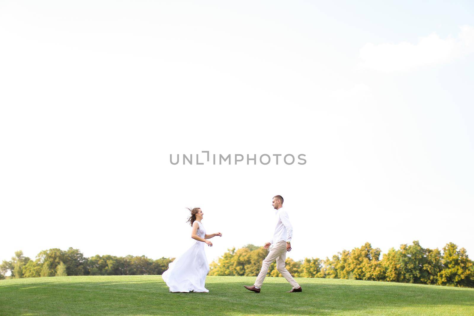 Happy bride and groom running to each other on grass in white sky background. Concept of wedding photo session on nature.