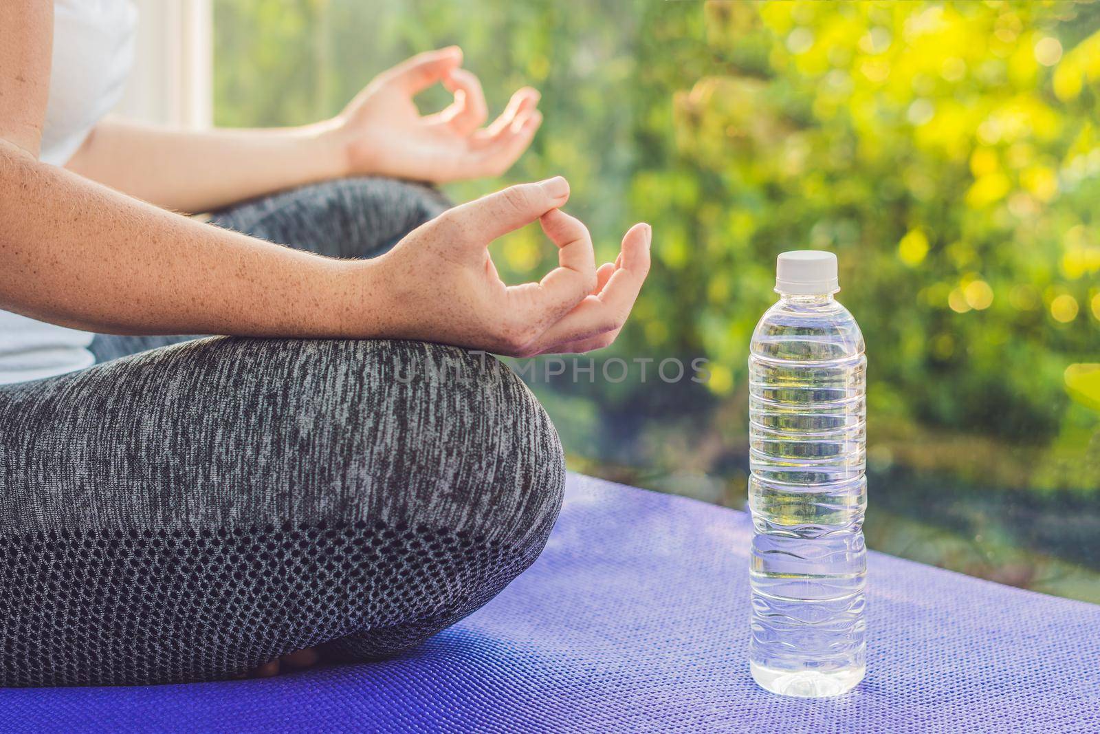 hand of a woman meditating in a yoga pose on a rug for yoga and a bottle of water by galitskaya