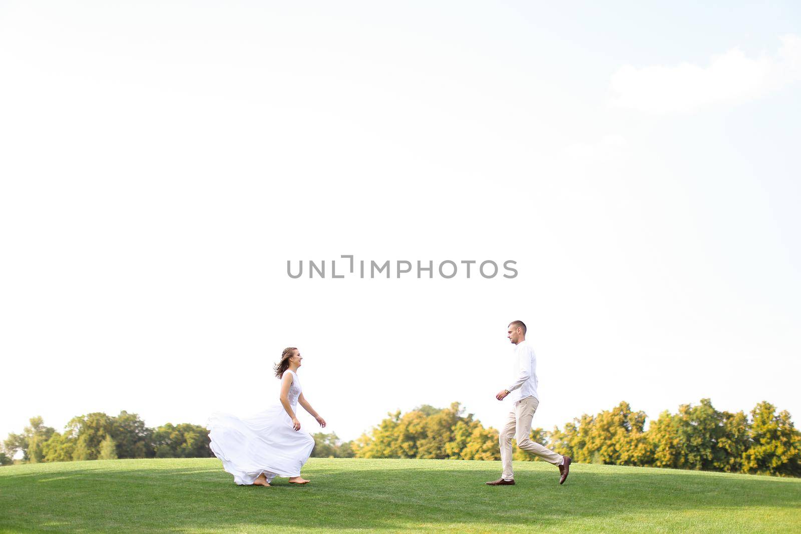 Bride and groom running to each other on grass in white sky background. Concept of wedding photo session on nature.