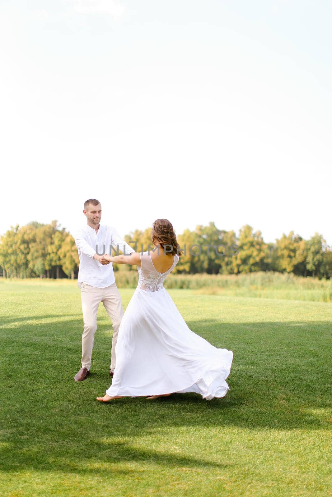 Happy groom and bride dress dancing on grass. Concept of wedding photo session on open air and nature.