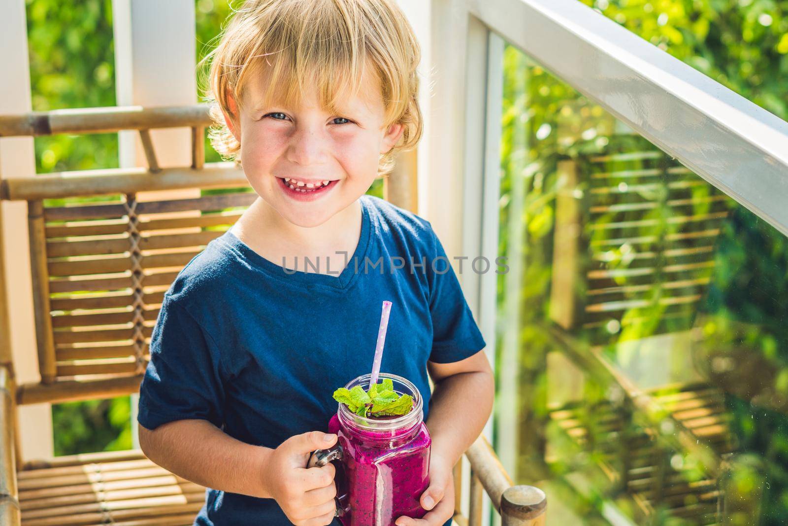 The boy holds smoothies from a dragon fruit with a mint leaf and a drinking straw.