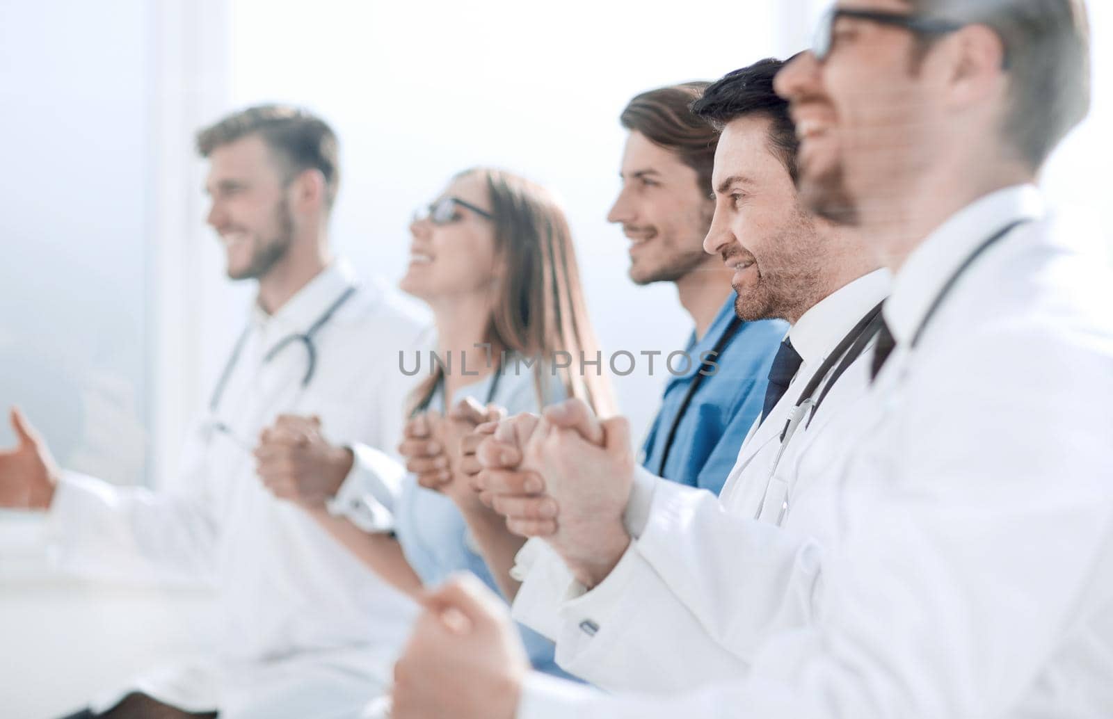 Happy group of people in white coats holding hands during a conference call.