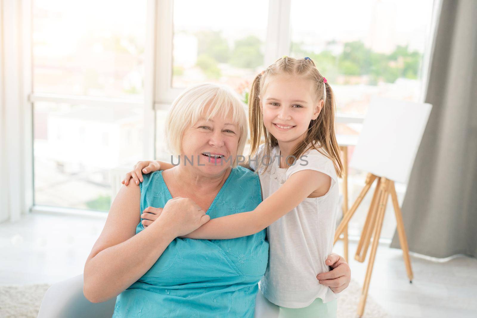 Cute little girl embracing smiling granny in light room