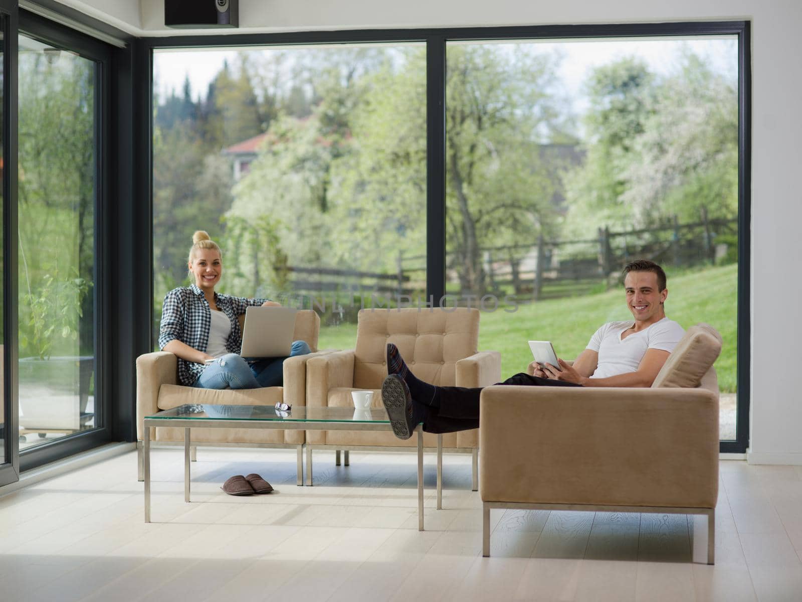 Young couple relaxing at luxurious home with tablet and laptop computers reading in the living room on the sofa couch.