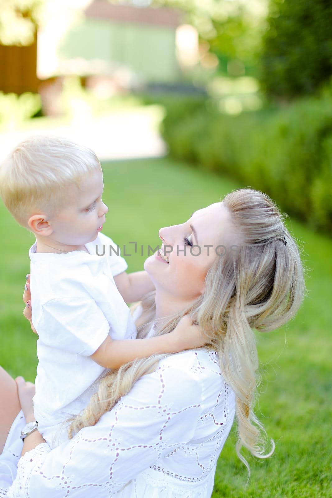 Young mother sitting and paying with little child on grass in yard. Concept of motherhood and summer vacations.