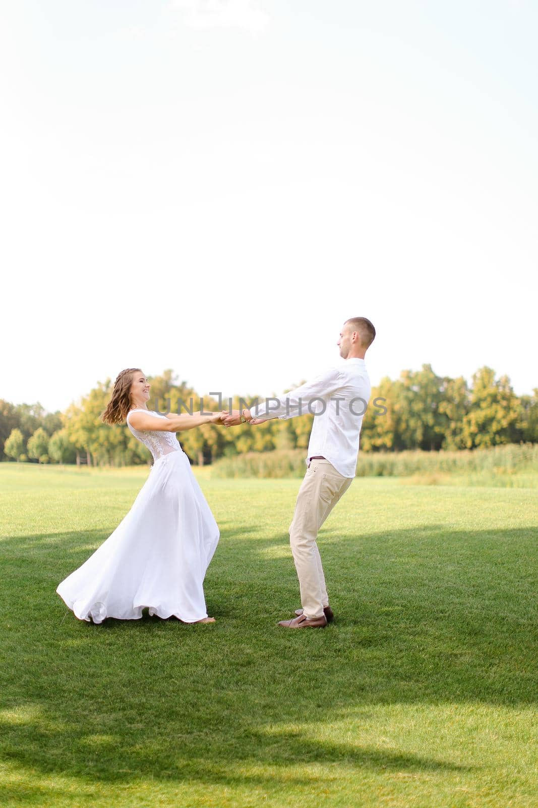 Happy european groom and bride dancing on grass. Concept of wedding photo session on open air and nature.