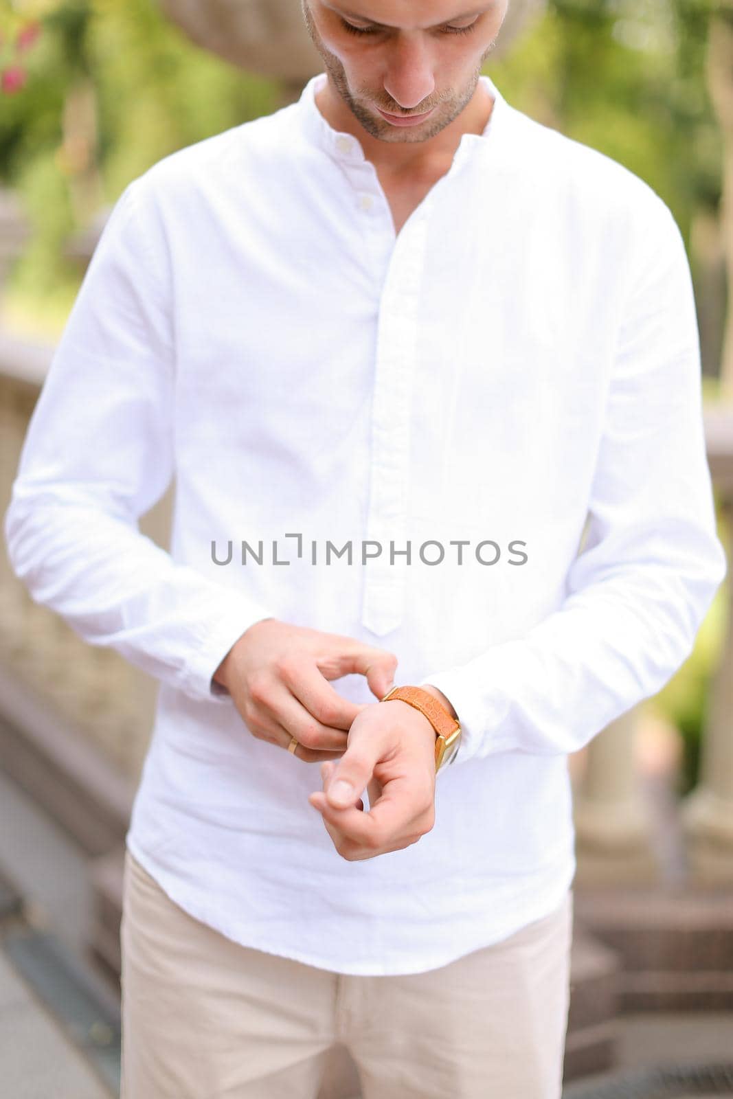 Caucasian groom looking at watch and waiting for bride outside. Concept of bridal photo session and young man.