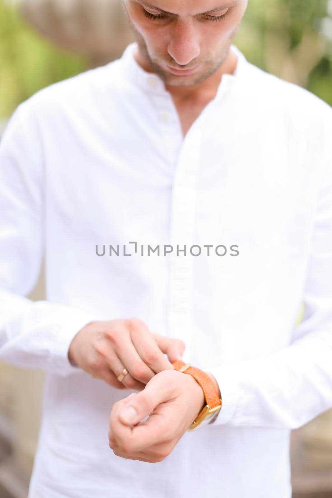 Caucasian happy groom looking at watch and waiting for bride outside. Concept of bridal photo session and young man.