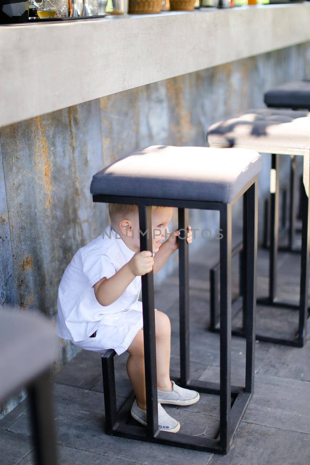 Little nice male baby wearing white clothes and playing outside at street cafe. Concept of childhood.