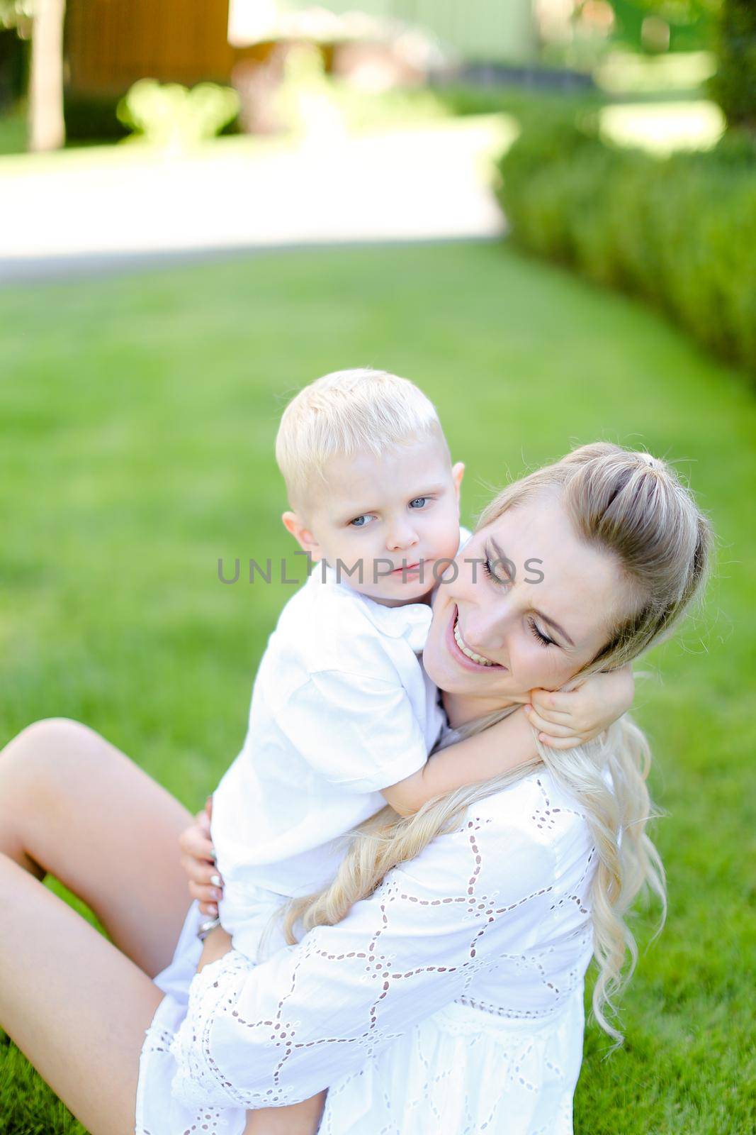 Young mom sitting with little child on grass in yard. Concept of motherhood and summer vacations.