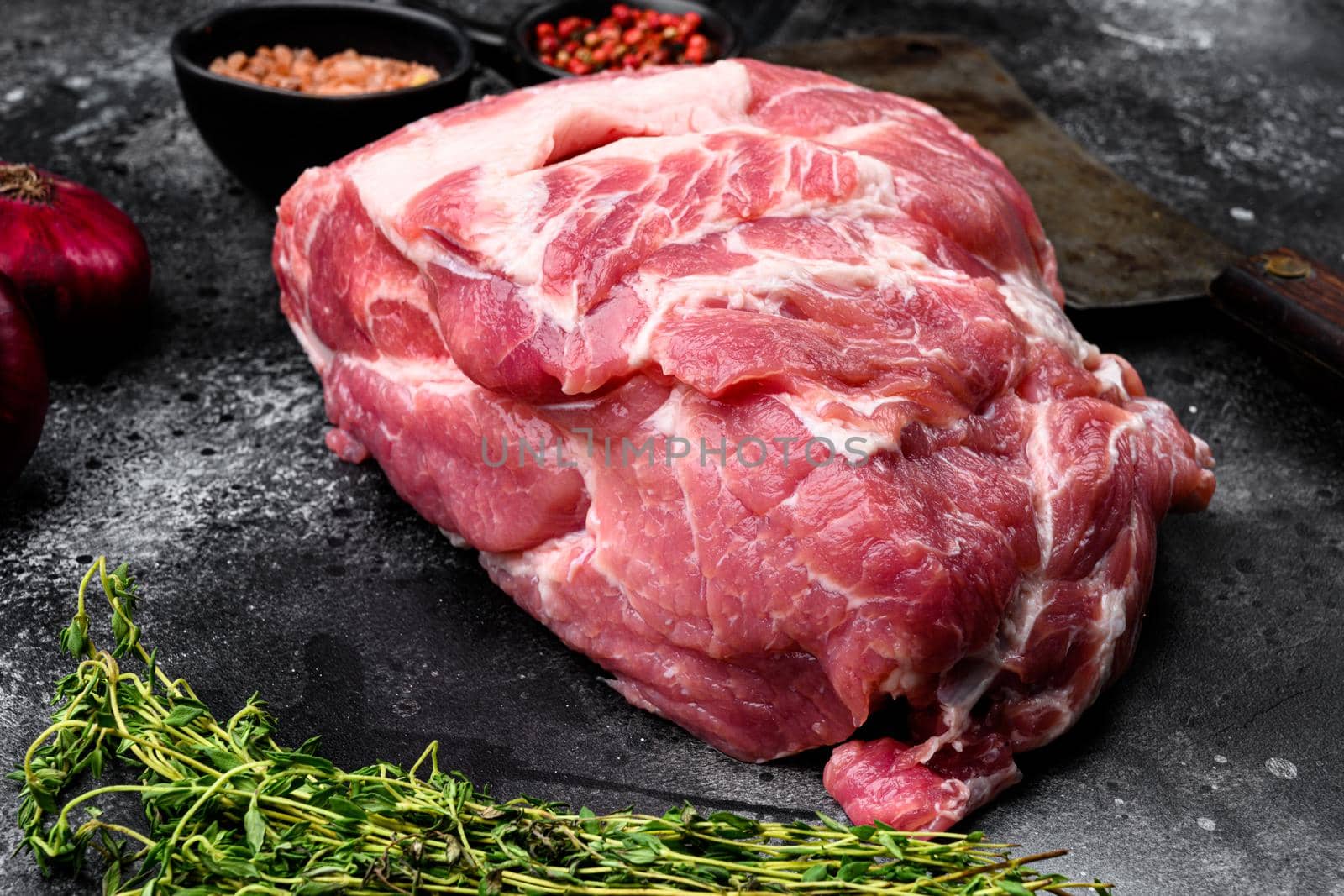 Raw pork neck meat piece for chop steak set, with ingredients and herbs, on black dark stone table background