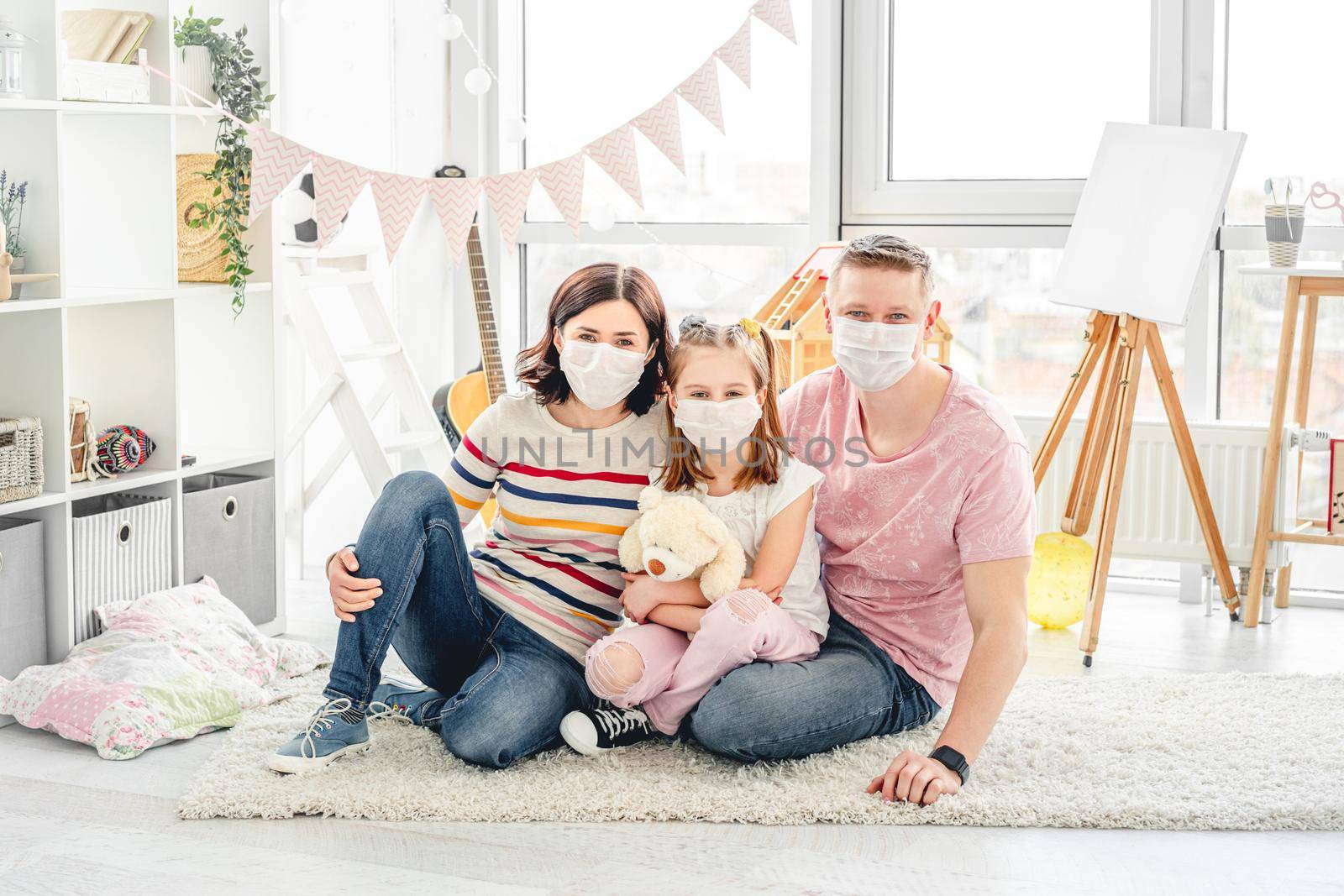 Beautiful family wearing medical masks sitting on floor in children's room