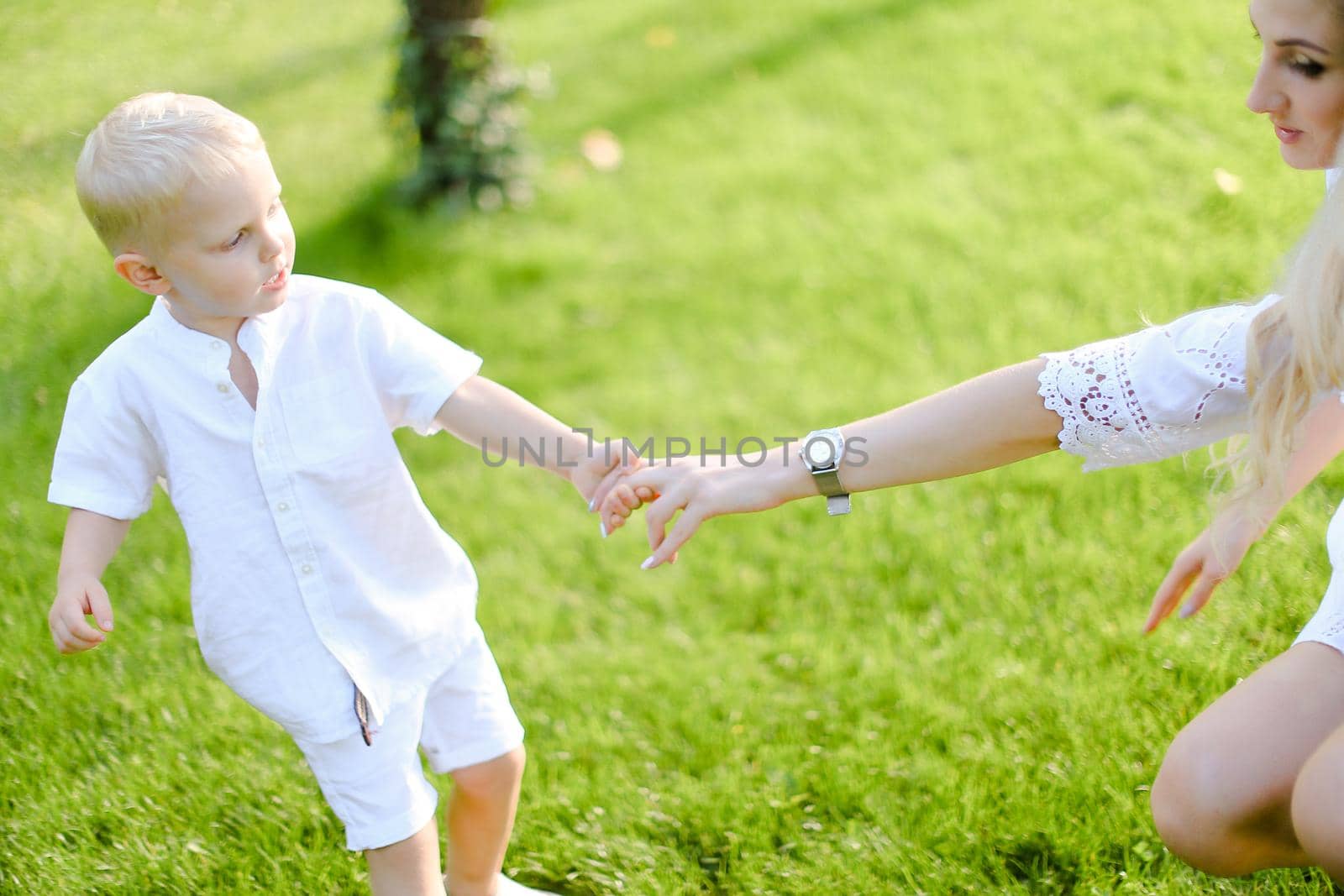 Young mother holding son hand in green grass background. by sisterspro