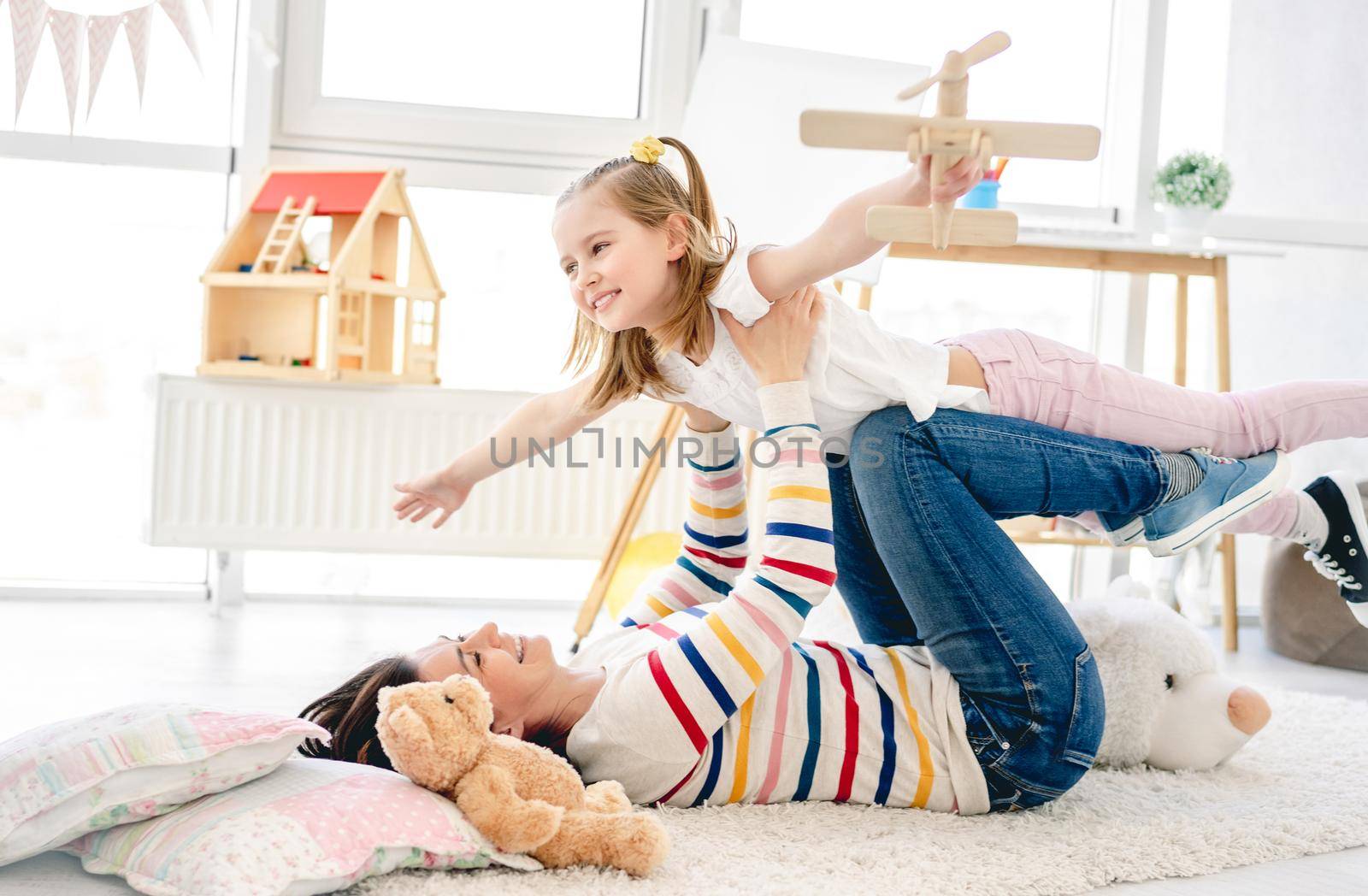 Happy girl with pretty mother playing in kids room