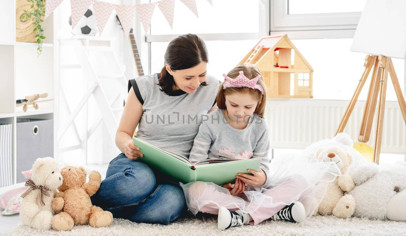 Lovely woman showing photo album to little girl in beautiful children's room