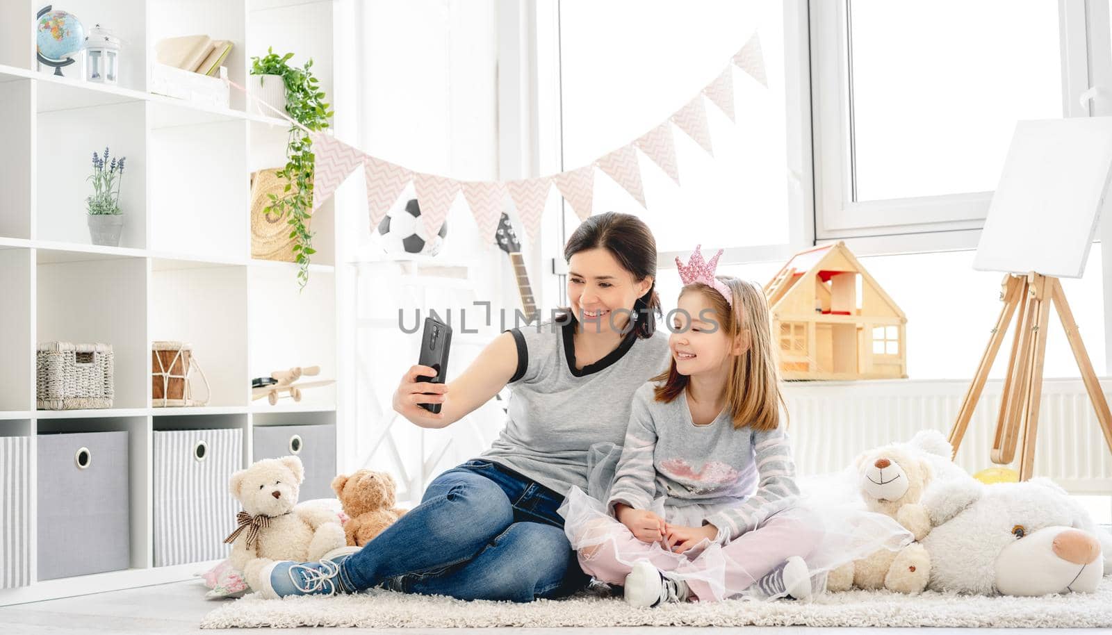 Smiling mother with daughter taking selfie in cute kids room