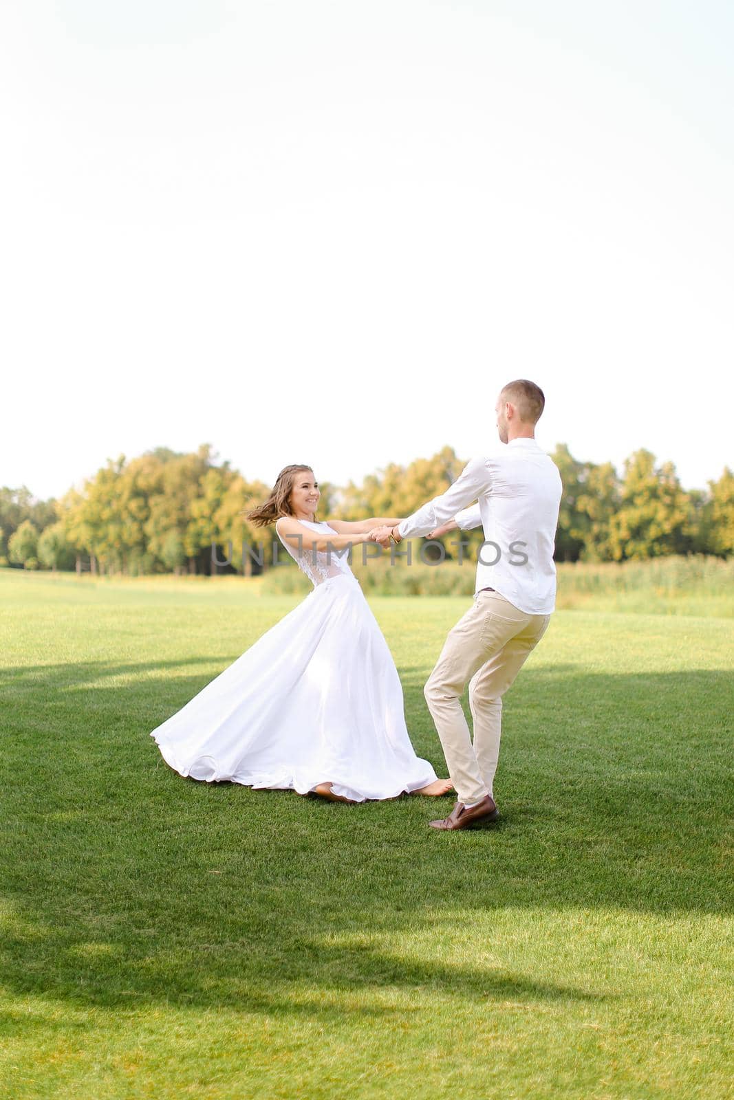 Happy caucasian groom and bride dancing on grass. Concept of wedding photo session on open air and nature.
