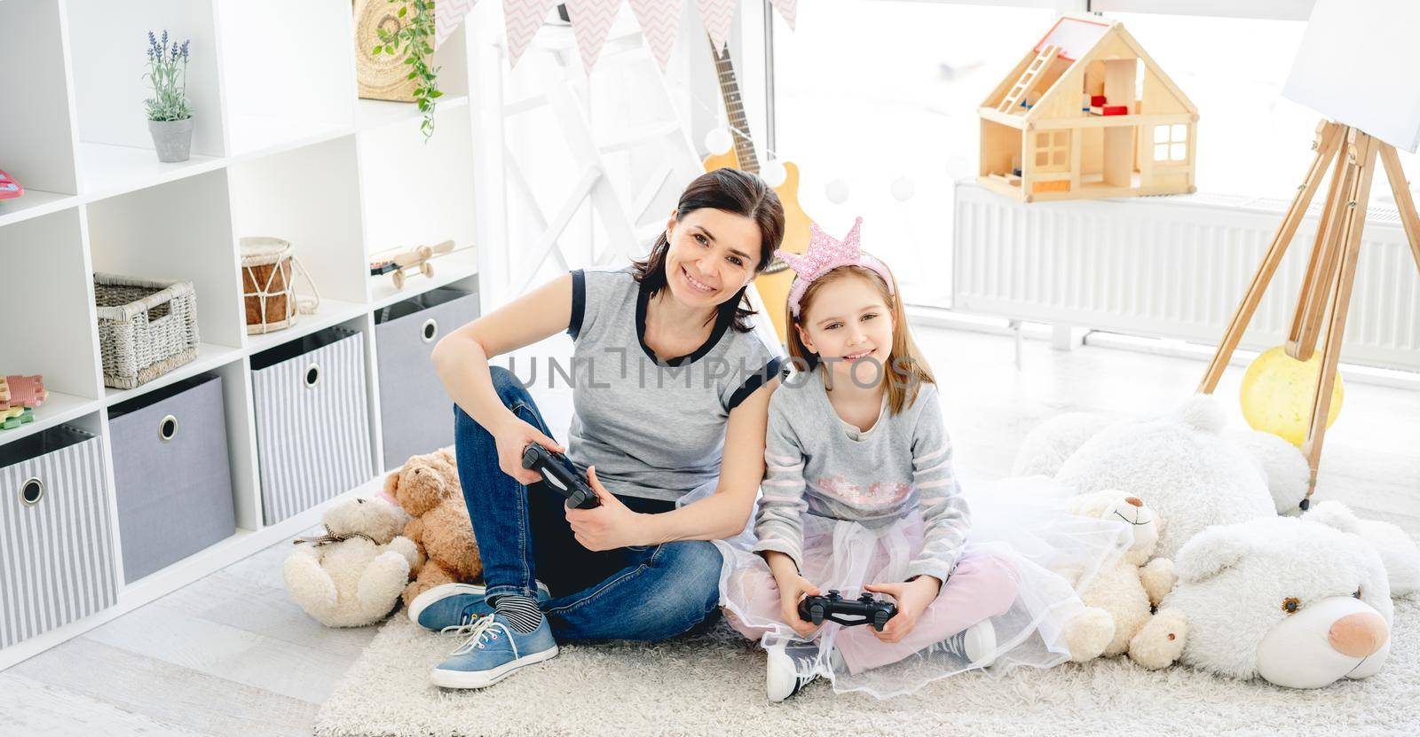 Cute little girl playing video game with mother in playroom