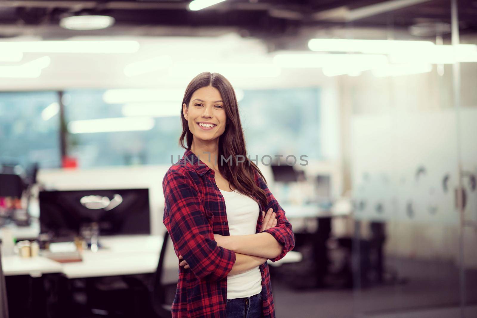 Portrait of young successful female software developer with with crossed arms at modern startup office