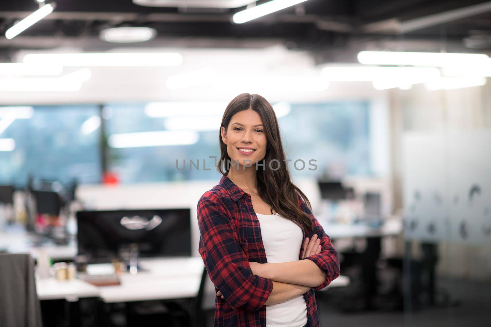 Portrait of young successful female software developer with with crossed arms at modern startup office