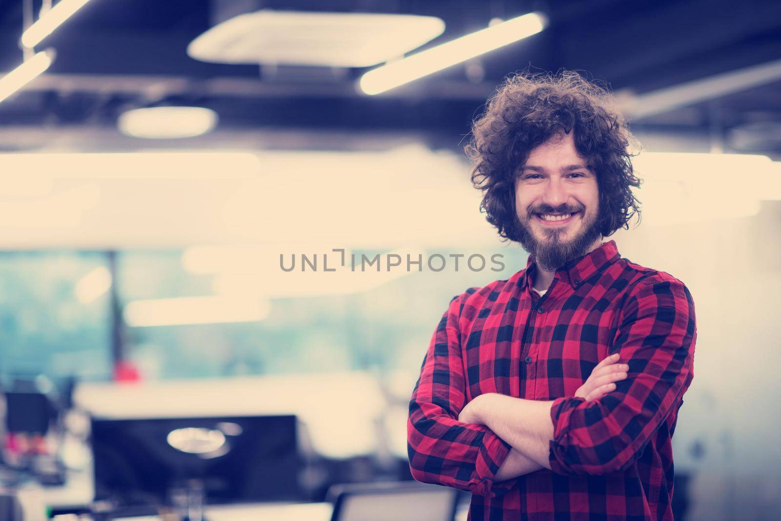 Portrait of young smiling successful male software developer standing at modern startup office