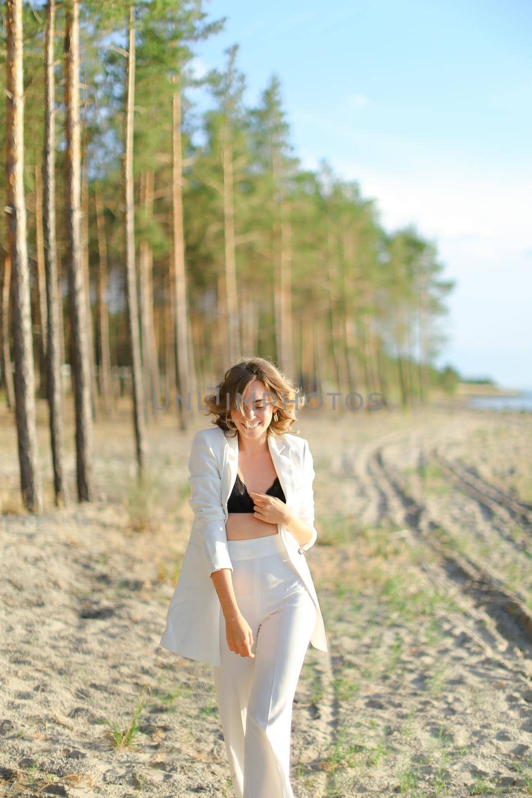 Pretty female person walking on sand beach and wearing white clothes. Concept of summer vacations.