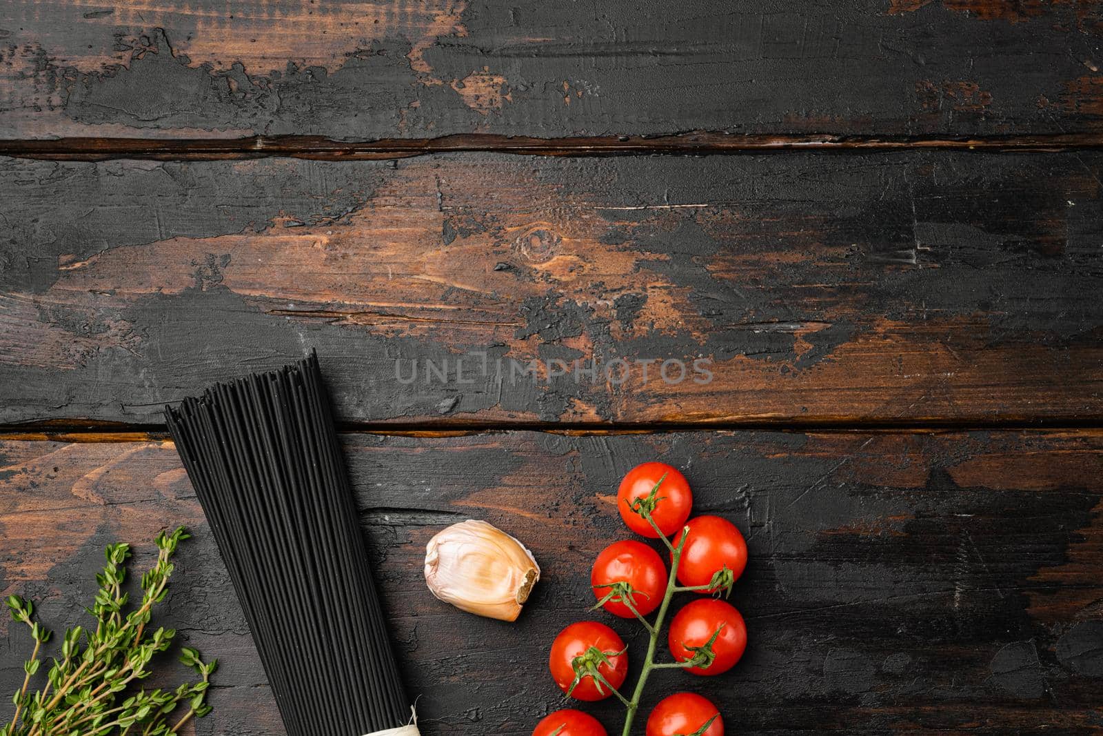 Uncooked black spaghetti and the ingredients set, on old dark wooden table background, top view flat lay, with copy space for text