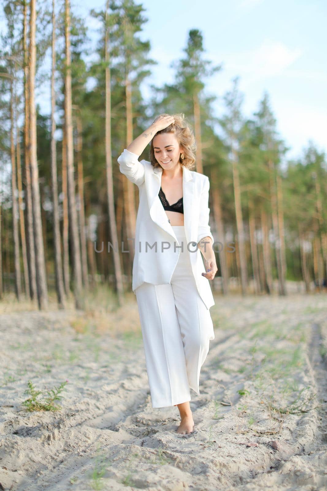 Blonde cute girl walking on sand beach and wearing white clothes. Concept of summer vacations.
