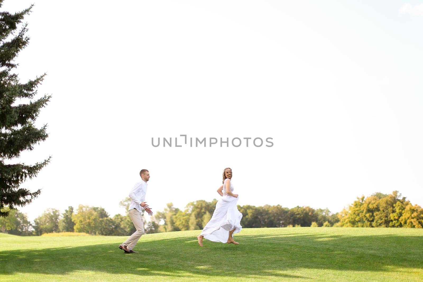 Groom and bride running and playing on grass. Concept of wedding photo session on open air and nature.