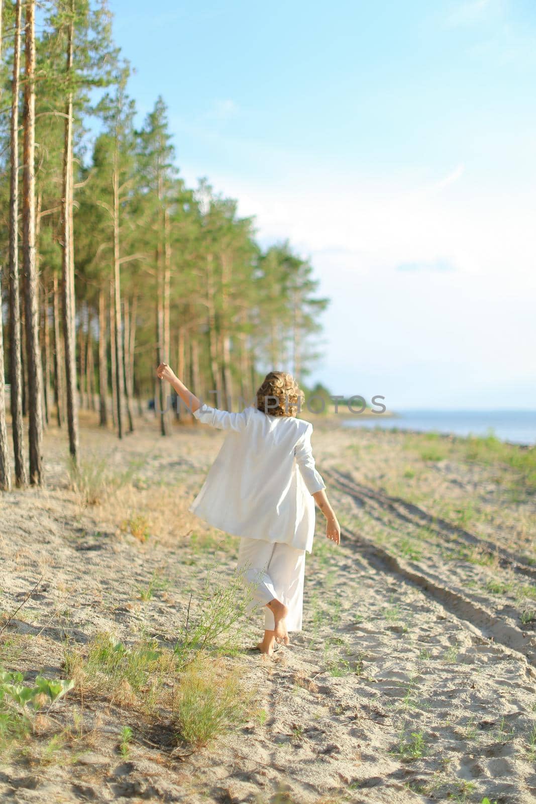 Back view of lady walking on sand beach and wearing white clothes. by sisterspro