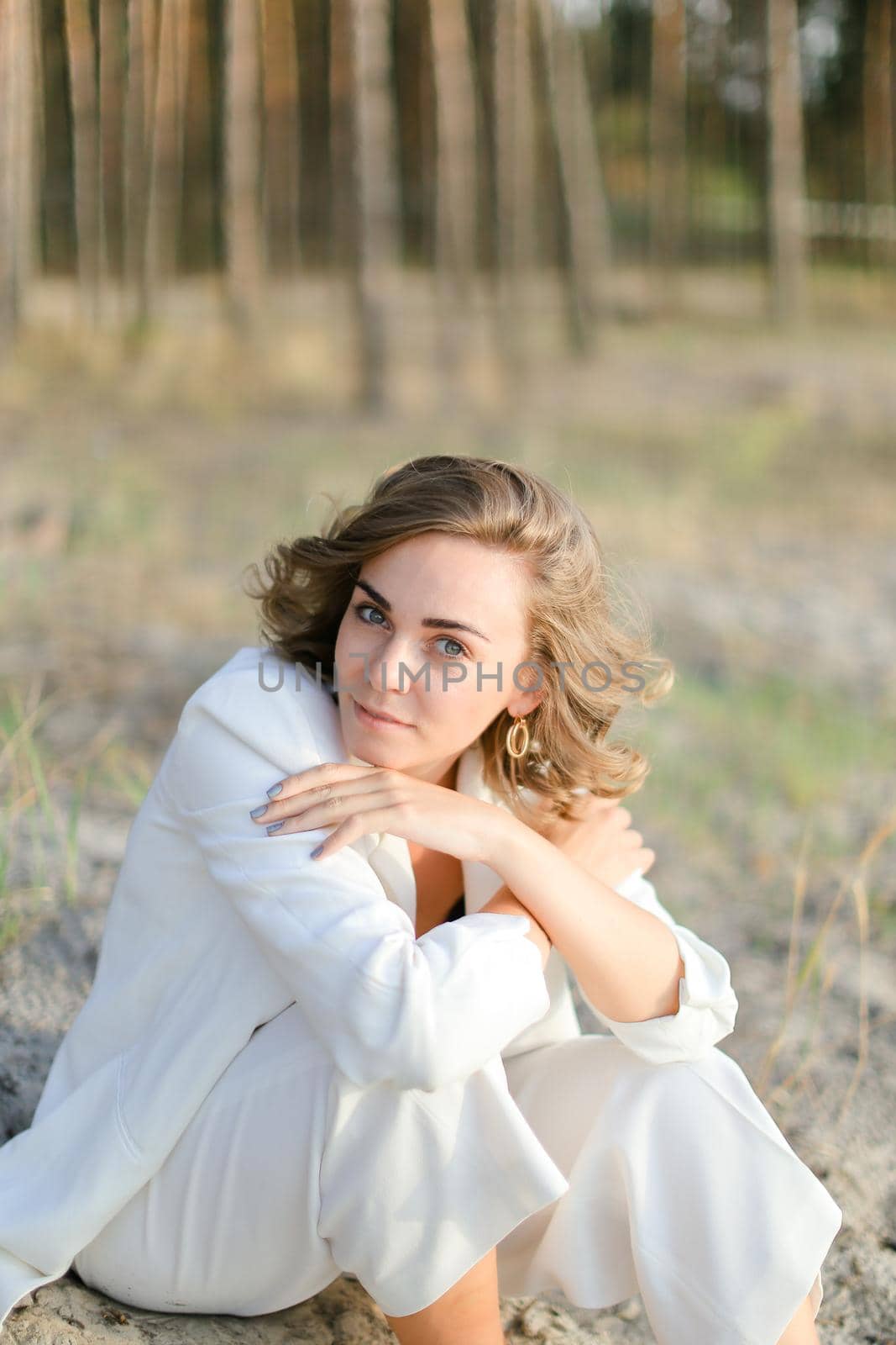 Young girl sitting on sand beach and wearing white clothes.