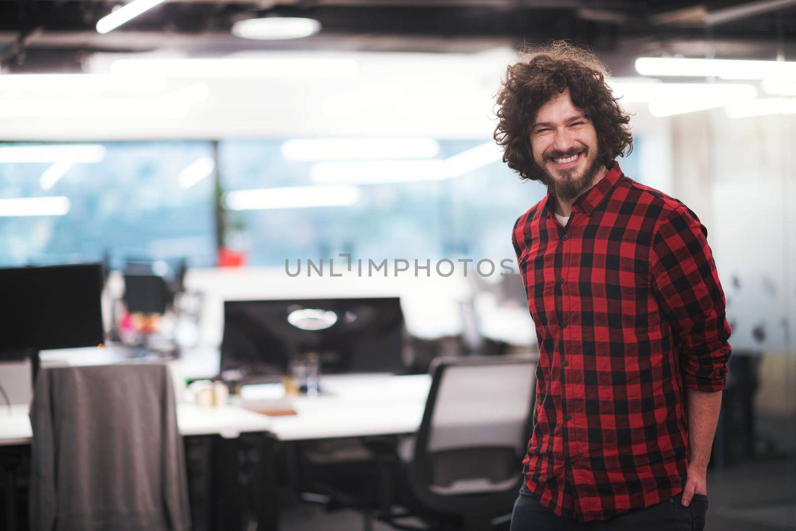 Portrait of young smiling successful male software developer standing at modern startup office