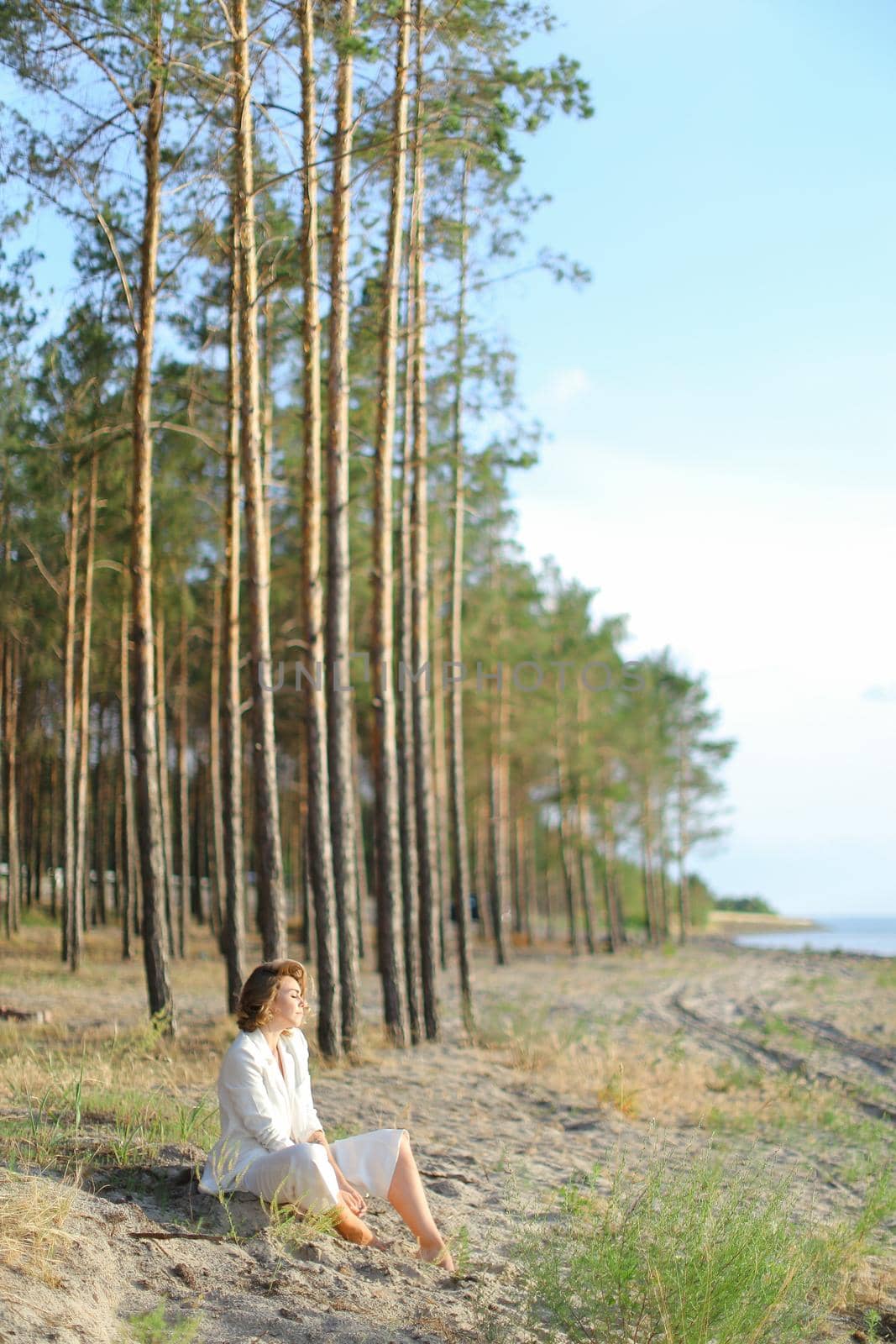 Young female person sitting on sand beach with trees in background. by sisterspro