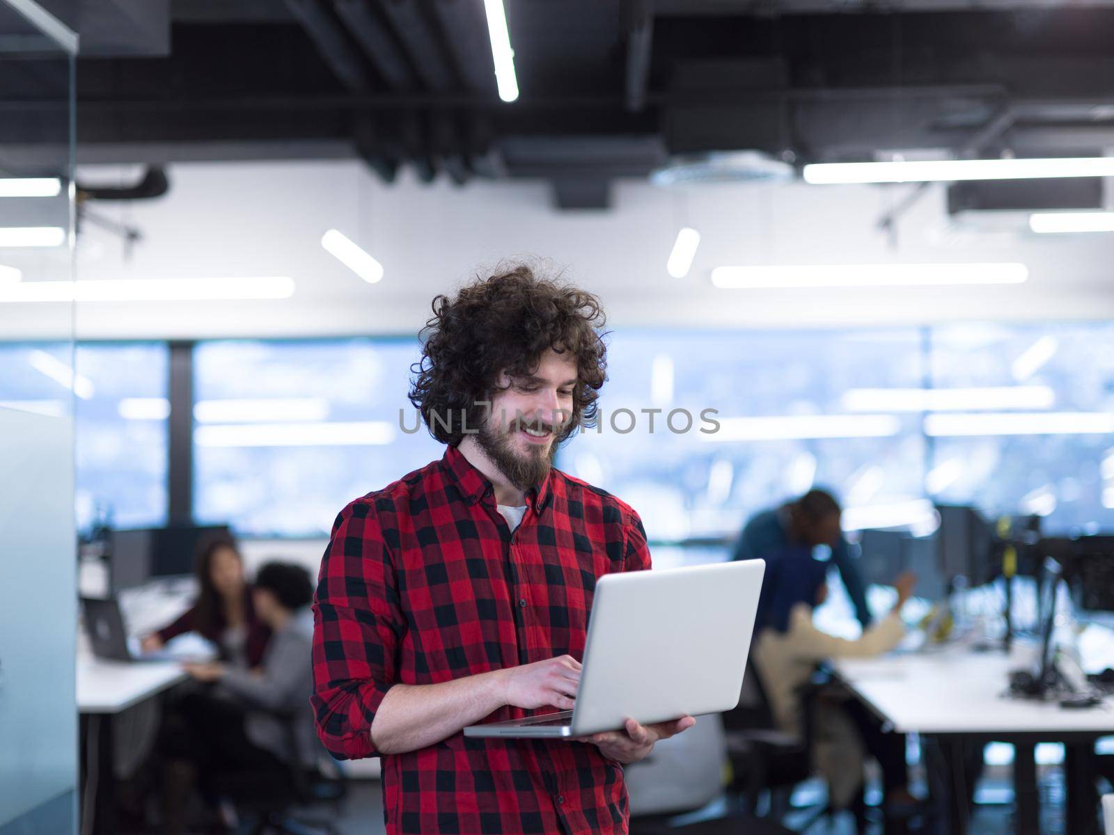 young smiling successful male software developer using laptop computer while standing at modern startup office