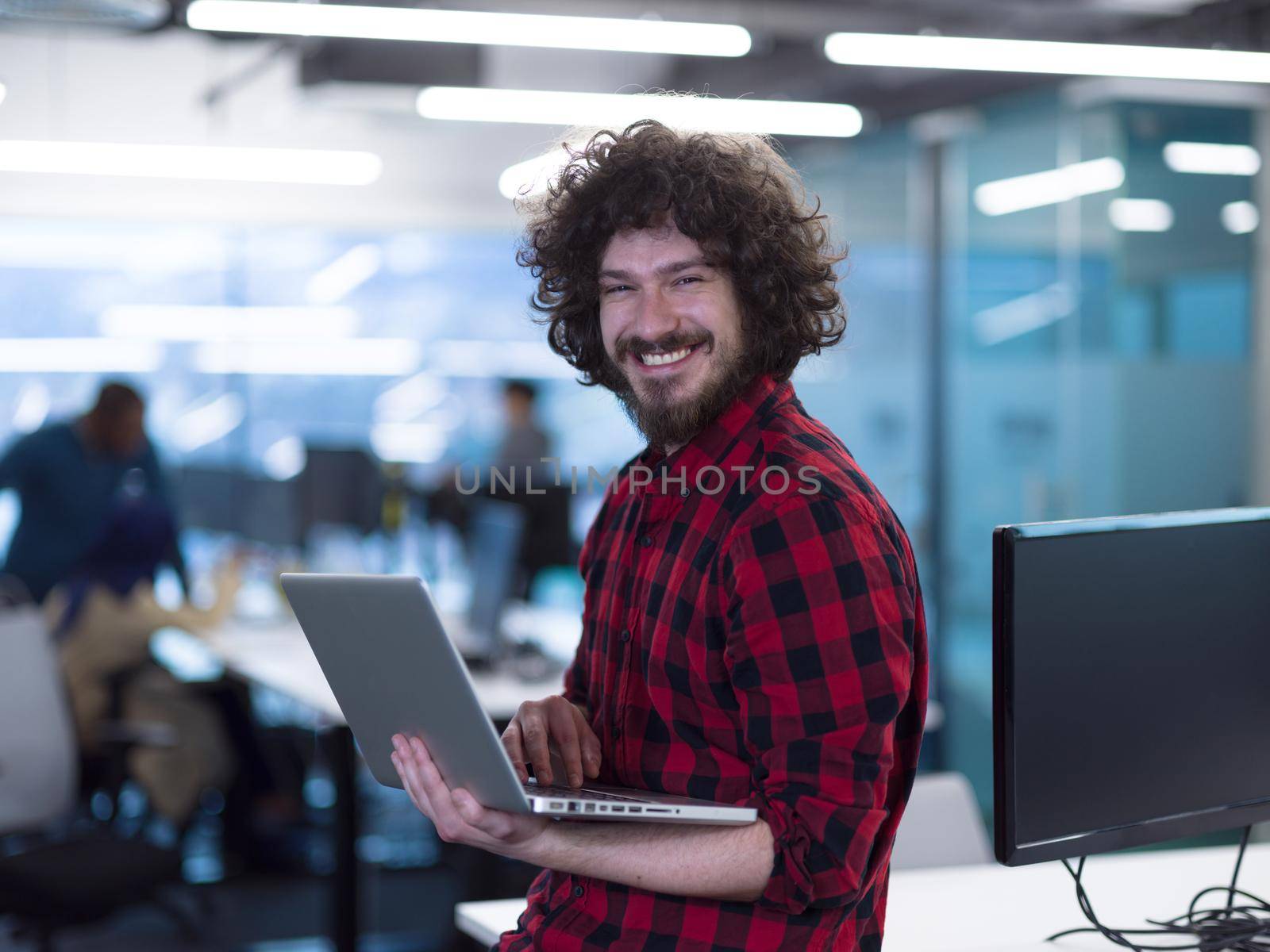 young smiling successful male software developer using laptop computer while standing at modern startup office