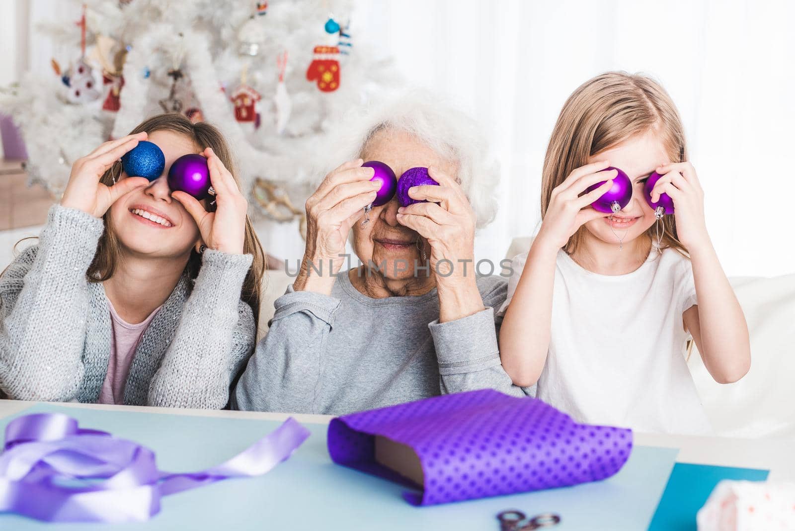 Smiling granddaughters playing with decorative balls like eyes with grandma at Christmas