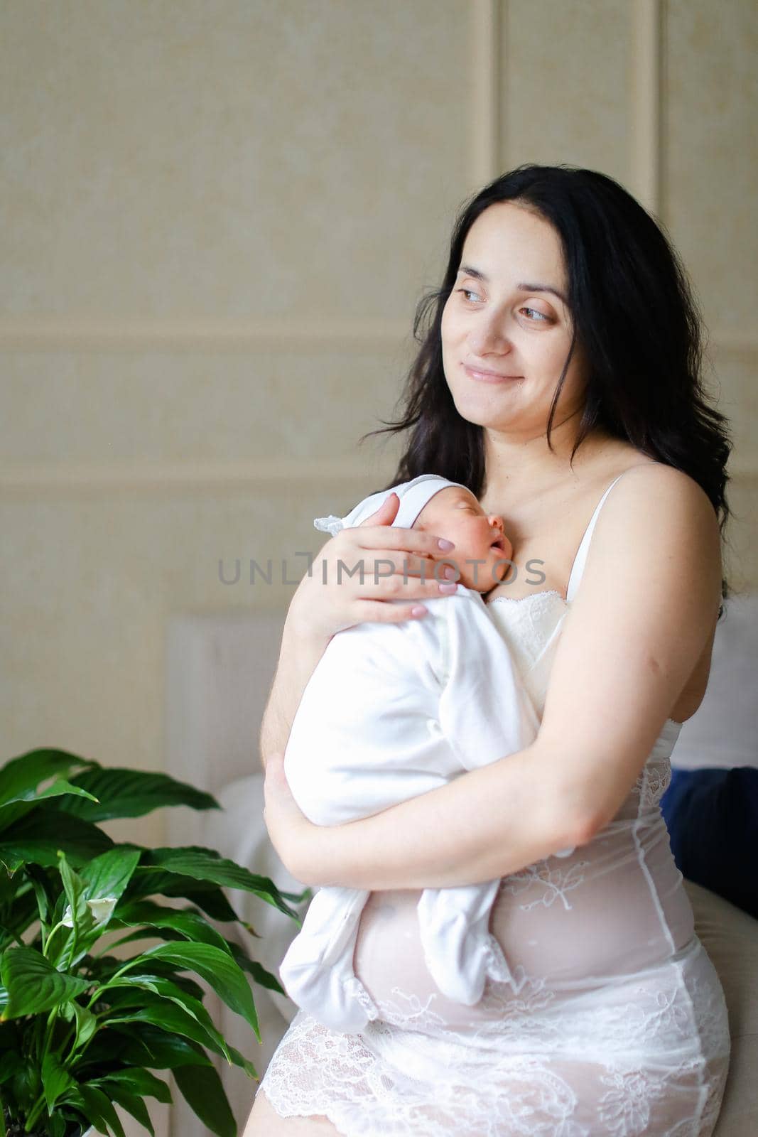 Young beautiful mother wearing white clothes holding newborn baby. Concept of motherhood and happiness.