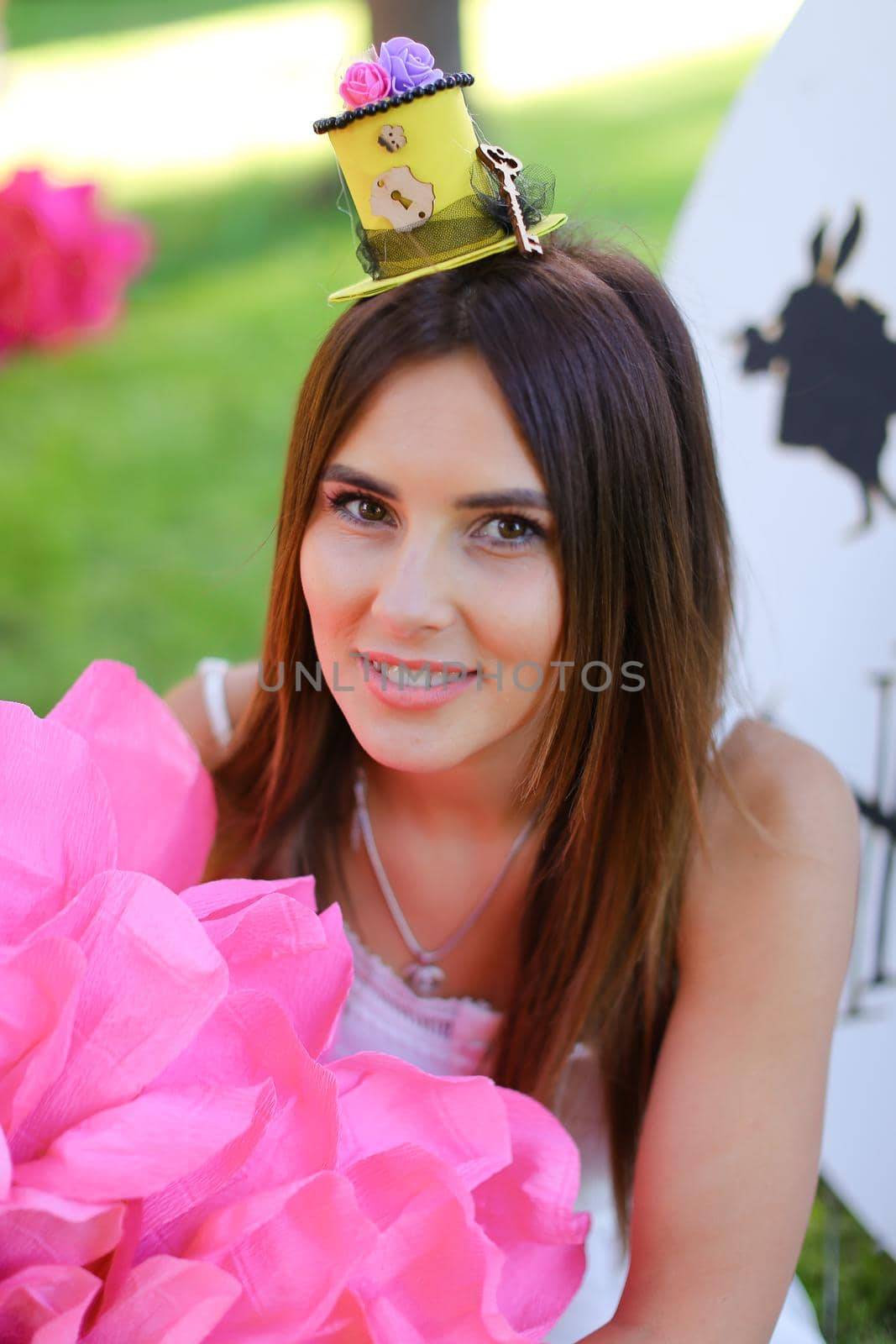 Young pretty girl sitting at decorated place for children near big pink flower. Concept of beauty and festive decorations.