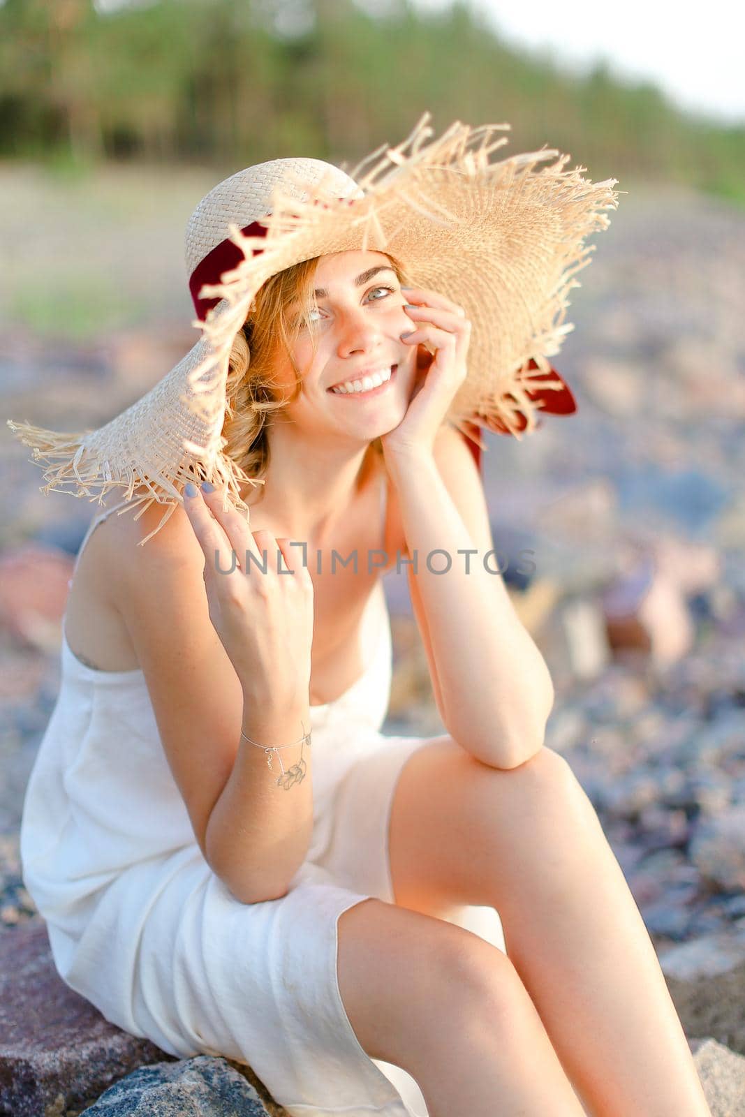 Young smiling woman in hat sitting on shingle beach. by sisterspro