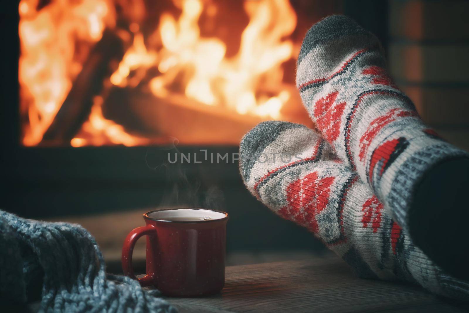 Girl resting and warming her feet by a burning fireplace in a country house on a winter evening. Selective focus by galsand