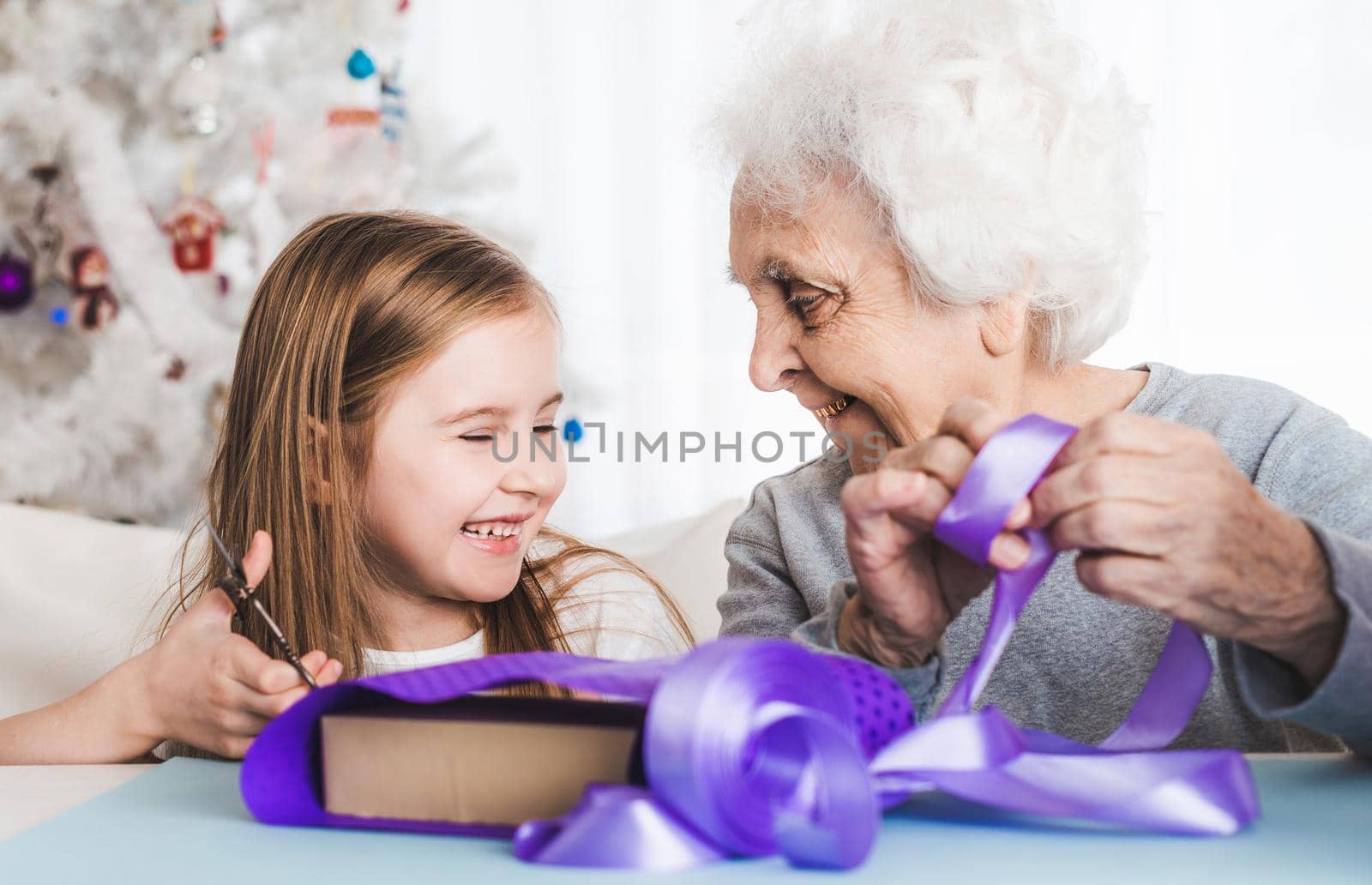 Smiling grandmother with little granddaughter decorating gifts together at Christmas