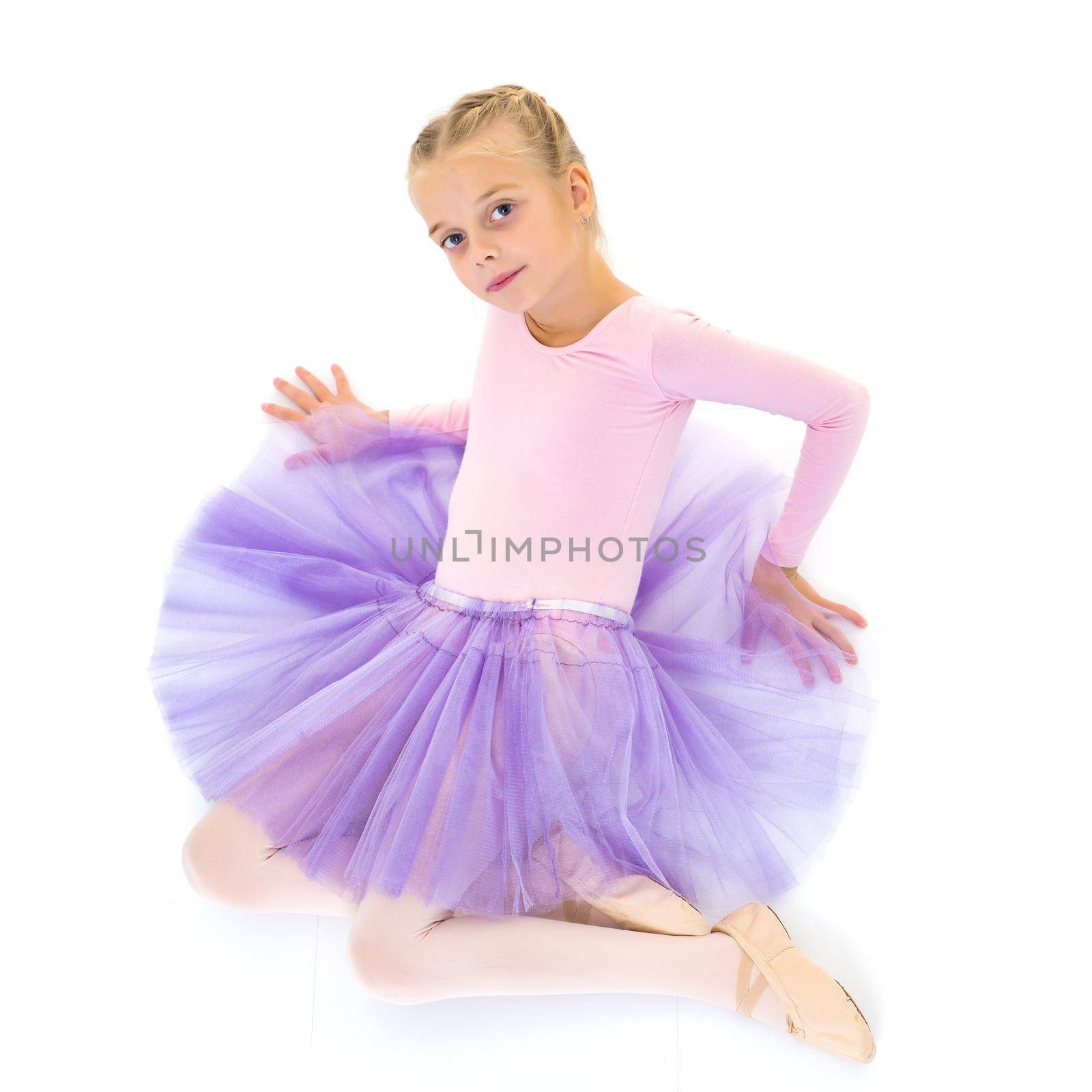 Charming little girl ballet dancer performing ballet poses on the floor in the studio on a white background.Isolated.