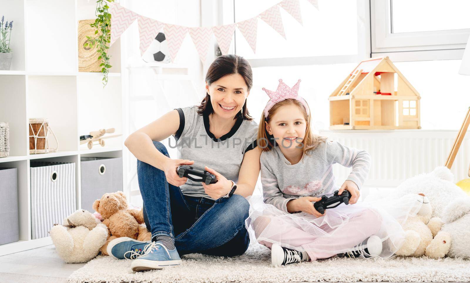 Happy mother and daughter playing video game in children room