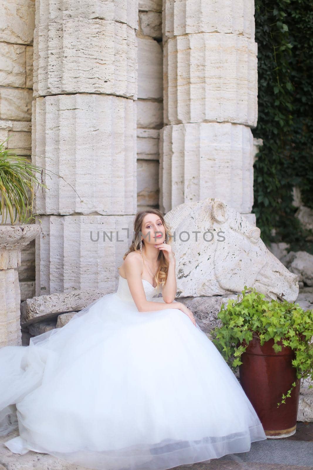 Caucasian bride sitting near ancient columns and wearing white dress. by sisterspro