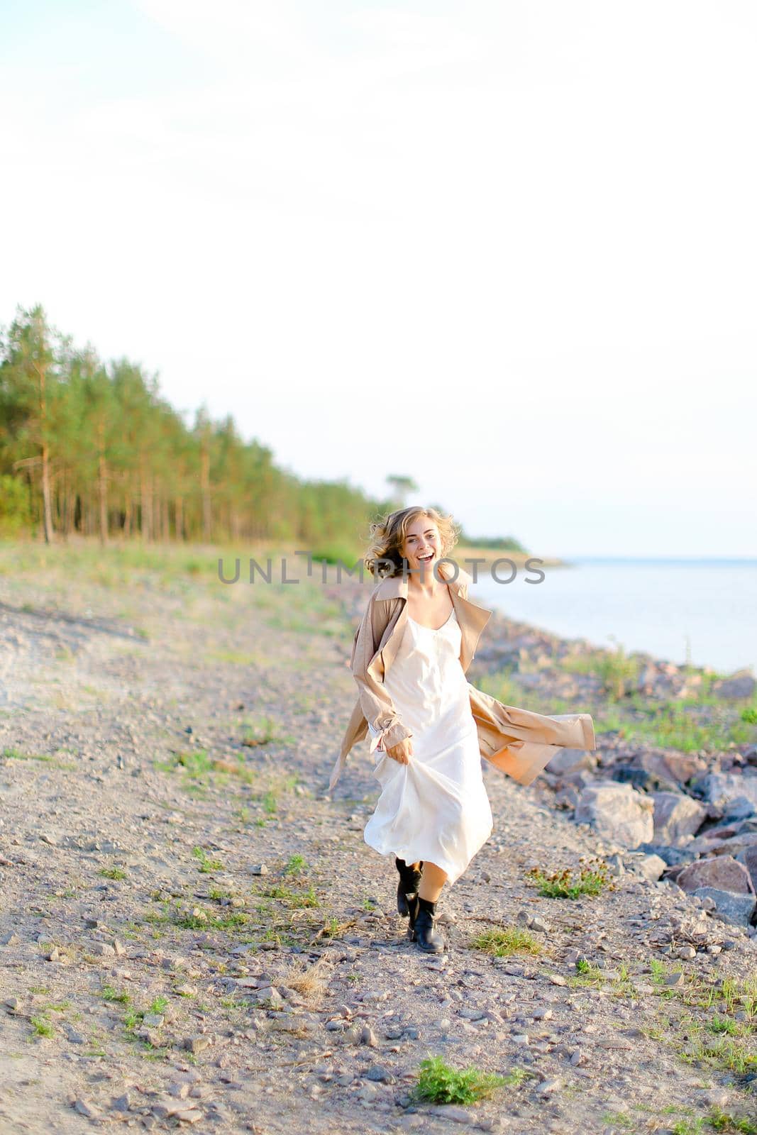 Young caucasian woman walking on shingle beach and wearing summer coat. by sisterspro