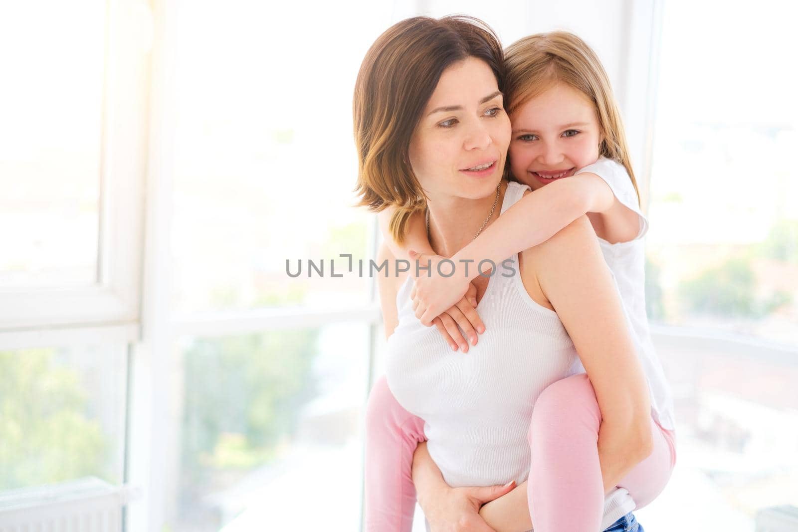 Mother with her little daughter girl playing in light room