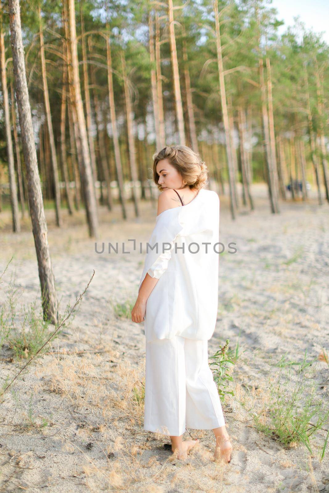 Back view of blonde woman in white walking on sand beach and wearing white clothes. by sisterspro