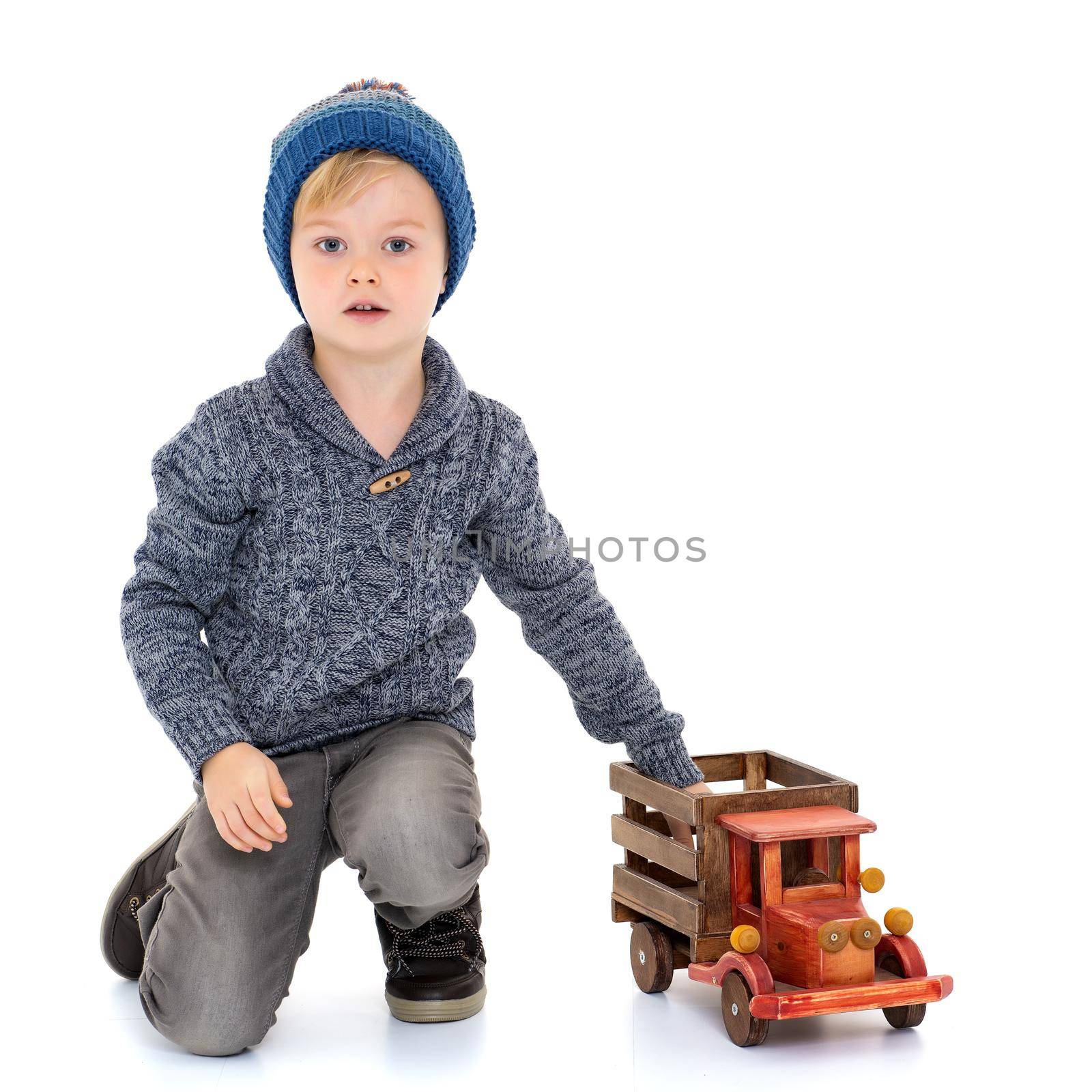 A cute little boy is playing with a big wooden car. The concept of development of a child in a family or a children's center. Advertising of children's goods and services. Isolated on white background.