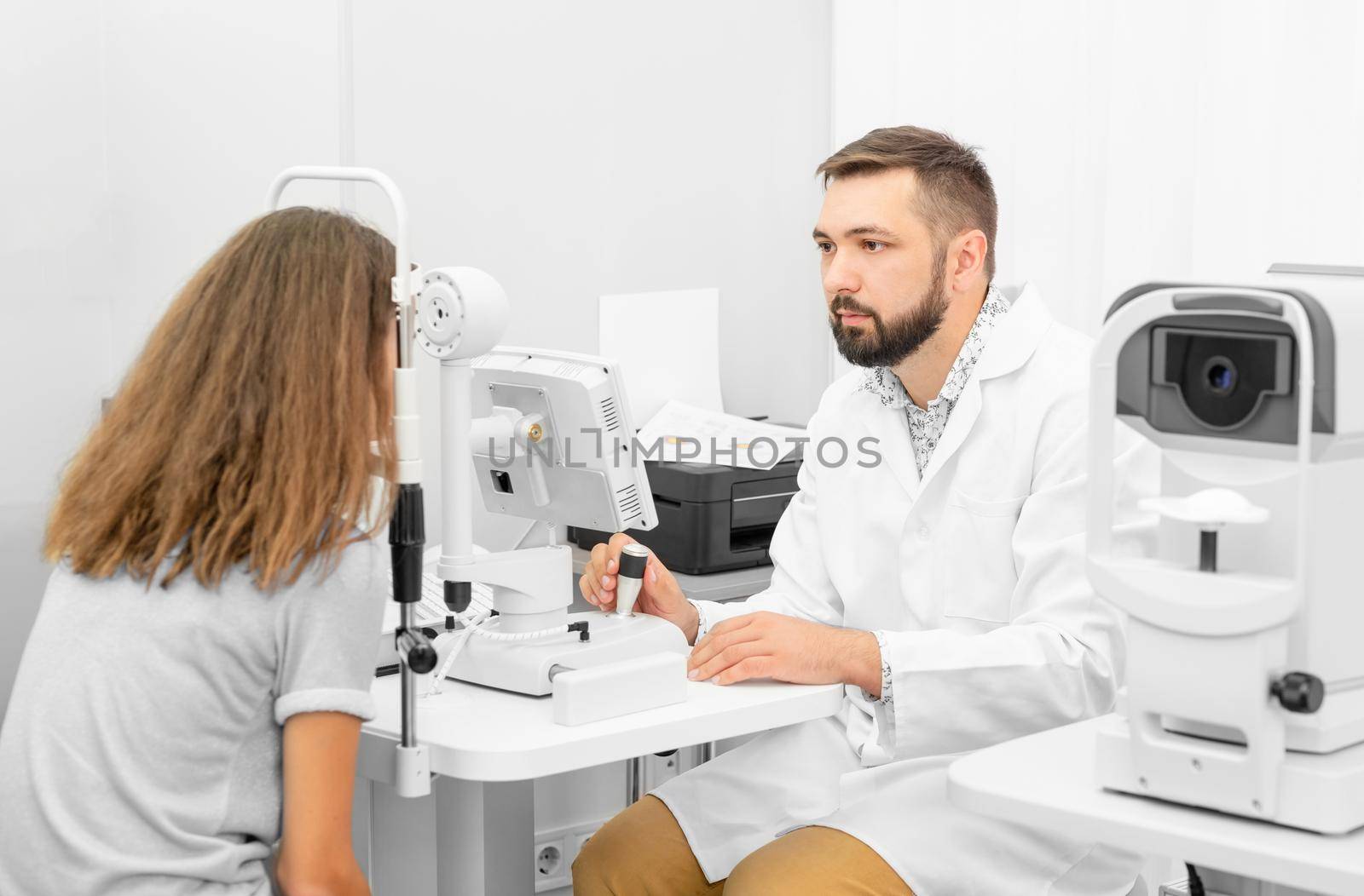 Doctor ophthalmologist holding equipment examinating teenager girl's eyes in the clinic