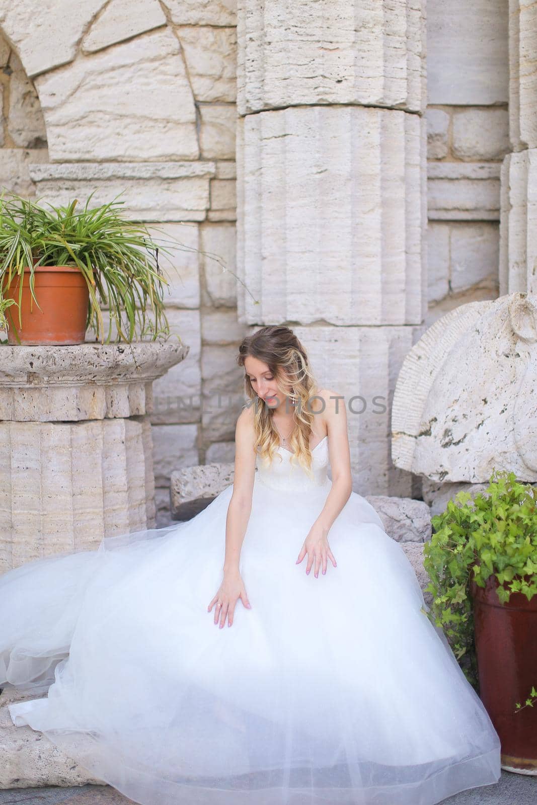 Caucasian american bride sitting near ancient columns and wearing white dress. by sisterspro